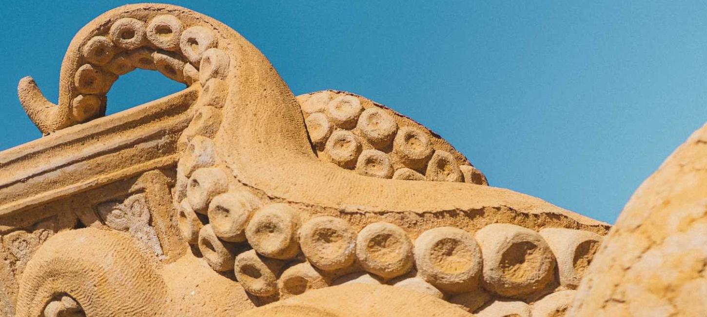 En blæksprutte i sand rækker tentaklerne mod himlen i Hundested Sandskulptur Park