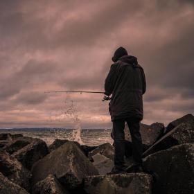 Mand står med ryggen til i blæsevejr og fisker i havet